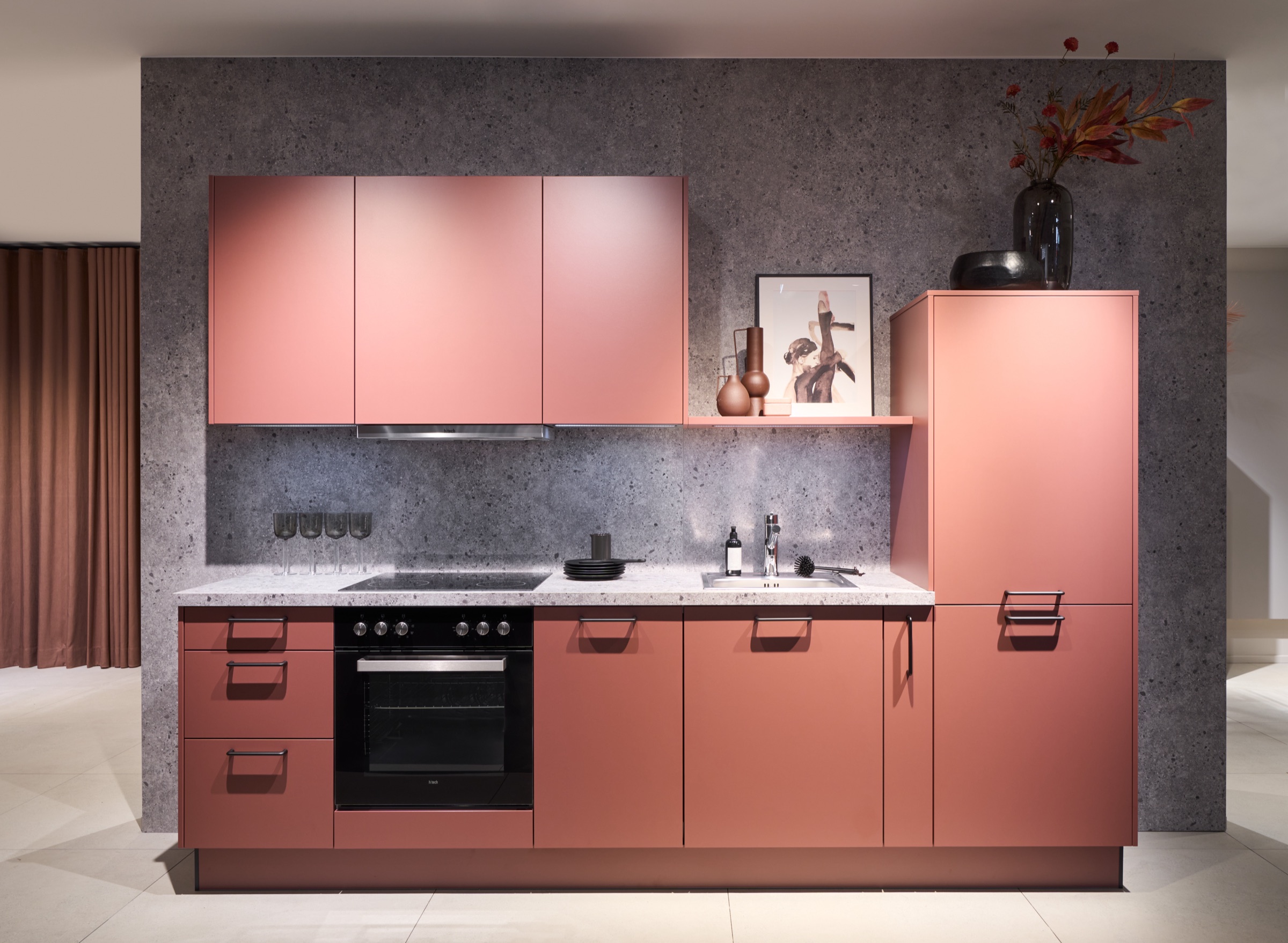 Küche in warmem Terracotta vor grauer Steinwand mit Kochfeld und Backofen – geplant vom Küchenstudio Ihre Schoene Küche in Berlin-Köpenick / Friedrichshagen
